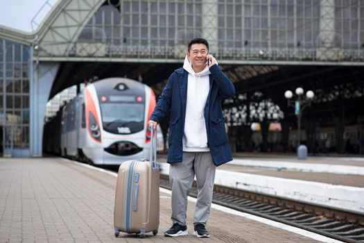 Business man Asian man at the train station having fun talking on the phone, a passenger arrived on a business visit to a new city, with a large suitcase of luggage