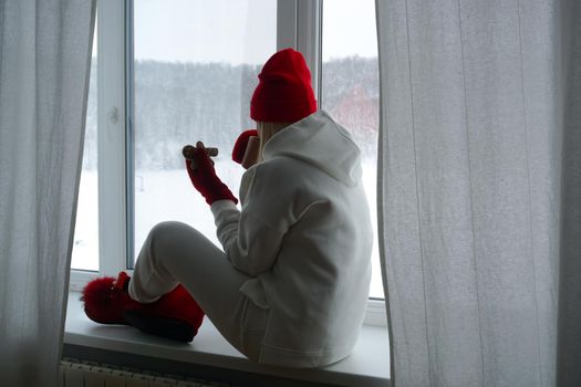 A woman in a white suit sits on the windowsill and looks out the winter window. High quality photo