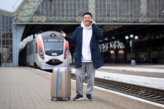 Business man Asian man at the train station having fun talking on the phone, a passenger arrived on a business visit to a new city, with a large suitcase of luggage