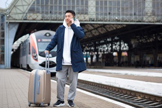 Business man Asian man at the train station having fun talking on the phone, a passenger arrived on a business visit to a new city, with a large suitcase of luggage