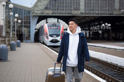 Man asian passenger arrives in nome town, with big suitcase, tourist at train station