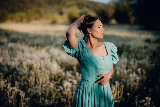 Portrait of young rural elegant woman posing on nature background. Sexy languid lady touching hair, enjoying summertime, sun rays. Vintage styled dress. High quality photo