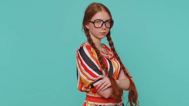 Offended redhead girl having misunderstanding, frustrated after quarrel, ignores and does not want to communicate, talk. Young angry teenager ginger child kid indoor isolated on blue studio background