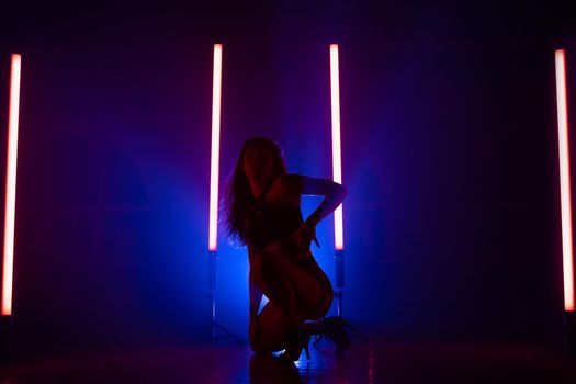 Sexy woman dancing on glowing led lamps background. She looks seductively. Blue smoky studio. High quality photo