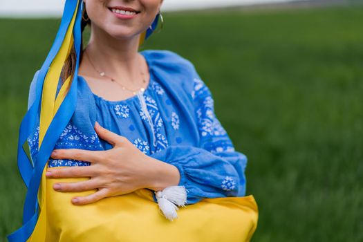 Smiling ukrainian woman with national flag on green field background. Young lady in blue embroidery vyshyvanka. Ukraine, independence, freedom, patriot symbol, victory in war. High quality photo