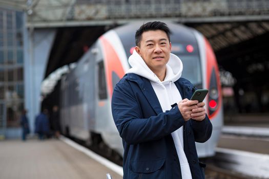 Male Asian businessman, at the train station, buys train tickets online, uses a mobile phone and an application, the tourist returns home from a business trip