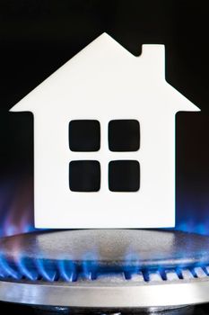 Heating season. The beginning of the heating season on natural gas. Concept, model of a house stands near the flame of a gas boiler on a black background. Home heating cost