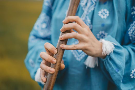 Woman playing woodwind wooden flute - ukrainian sopilka outdoors. Folk music, culture concept. Musical instrument. Lady in traditional embroidered shirt - blue vyshyvanka. High quality photo