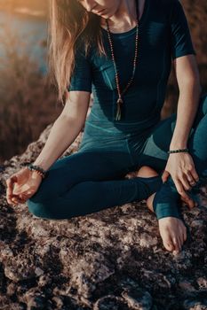 Yogi woman sitting in mala beads with gyan mudra, meditating, feeling free in front of wild nature. Mindful fitness coach having zen moment. Everyday yoga practice, calm breath, concentration.