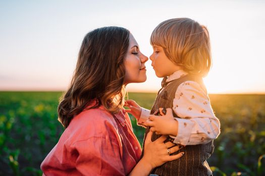 Tender scene of loving son with mom on sunset backdrop. Beautiful family. Cute 3 year old kid with mother. Parenthood, childhood, happiness, children wellbeing concept. High quality photo