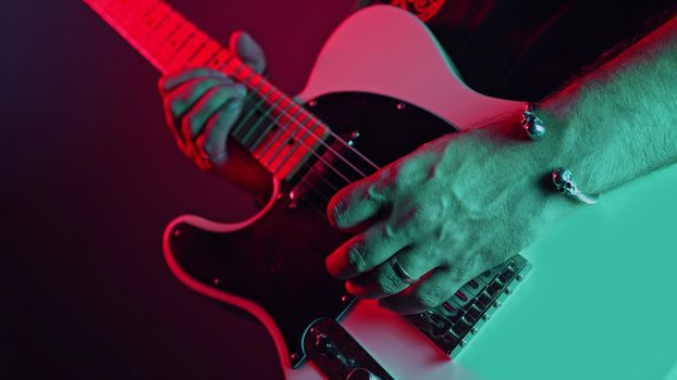 Rock guitarist man on smoky stage masterfully playing electrical guitar. Musician plays music during concert under neon colorful light. High quality photo