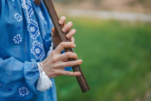 Woman playing woodwind wooden flute - ukrainian sopilka outdoors. Folk music, culture concept. Musical instrument. Lady in traditional embroidered shirt - blue vyshyvanka. High quality photo