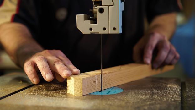 Handwork, carpentry concept, woodworking. Carpenter working in in factory atelier. Joiner labourer cuts wooden plank on jigsaw machine. High quality photo