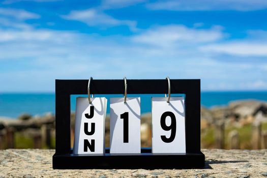 Jun 19 calendar date text on wooden frame with blurred background of ocean. Calendar date concept.