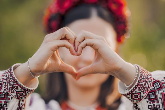 Ukrainian woman in traditional embroidery vyshyvanka dress making sign of shape heart. Ukraine, volunteering, donation help and love concept. High quality photo