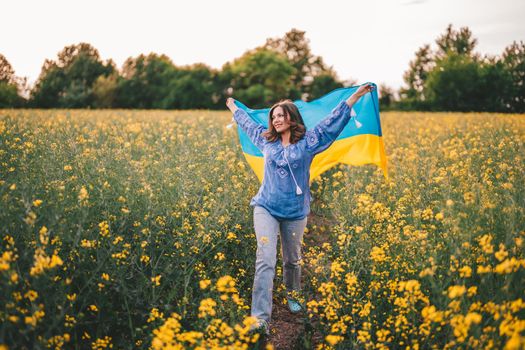 Ukrainian patriot woman running with national flag in canola yellow field. Ukraine, peace, independence, freedom, victory in war. High quality photo