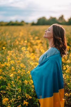 Pretty ukrainian patriot woman with national flag in canola yellow field. Ukraine unbreakable, peace, independence, freedom, victory in war. High quality photo