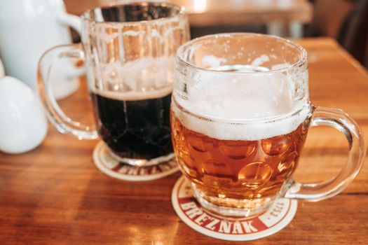 Prague, Czech Republic - July 2022. Two mugs of white and dark Breznak beer in pub. High quality photo