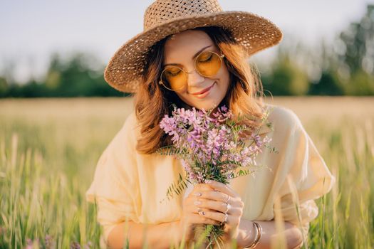 Portrait of happy woman in straw hat in fresh green wheat field. Grass background. Amazing nature, farmland, growing cereal plants. Stylish lady with eyewear. High quality photo