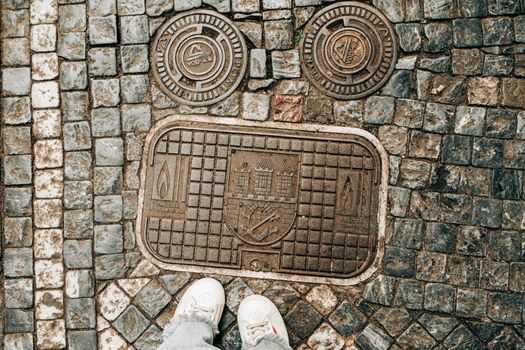 Female legs in white sneakers on paving stones with czech sewer hatches. Teenage feet top view. Prague street, old city. High quality photo