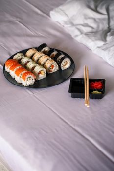 A plate with a sushi set stands on a white bedspread, rolls for a romantic dinner. Traditional japanese food