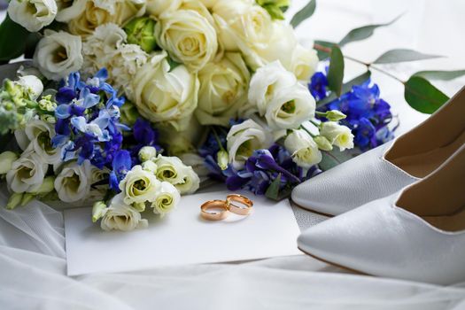 Wedding shoes for the bride. White high-heeled shoes near wedding rings, wedding jewelry. Marriage concept