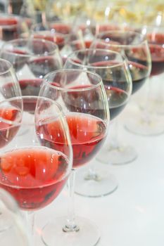 A large number of glass goblets filled with red wine are neatly arranged on the banquet table for the celebration. Wine is a type of alcoholic beverage.
