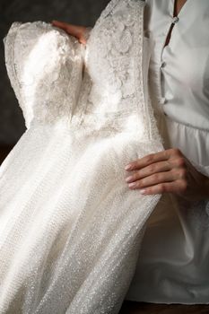 The bride holds a white dress in her hands on the wedding day.