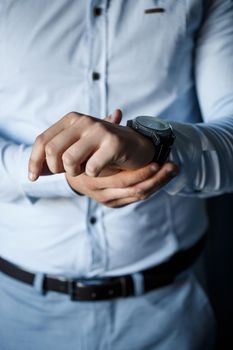 A man elegant businessman buttons a watch on his hand he is dressed in a white dress shirt