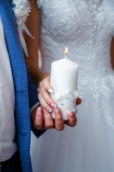 Burning candle in the hand of the newlyweds