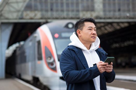 Male Asian businessman, at the train station, buys train tickets online, uses a mobile phone and an application, the tourist returns home from a business trip