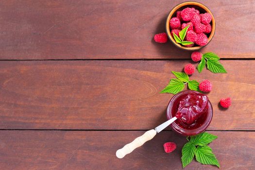 fresh raspberry jam in a glass jar on a wooden table, next to fresh raspberries. concept of homemade jam, preserves for winter, selective focus and copy space