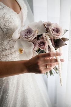 Beautiful bride holding a delicate bouquet of flowers in her hands on a wedding day