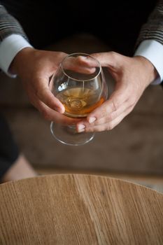 A man businessman holds a glass with alcohol in his hand. Dressed in a jacket and shirt. Rest after a working day