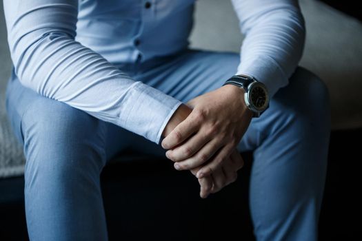 A man elegant businessman buttons a watch on his hand he is dressed in a white dress shirt
