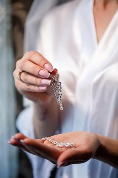 The bride holds earrings in her hand on her wedding day. Jewelry for a holiday for the newlyweds