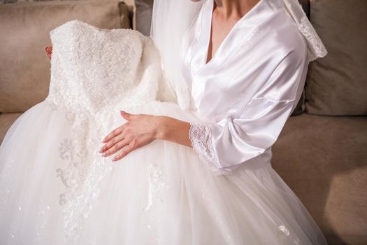 The bride holds a white dress in her hands on the wedding day.