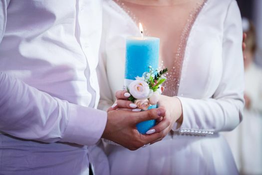 Burning candle in the hands of the newlyweds