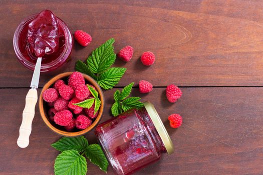 fresh raspberry jam in a glass jar on a wooden table, next to fresh raspberries. concept of homemade jam, preserves for winter, selective focus and copy space