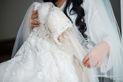 The bride holds a white dress in her hands on the wedding day.