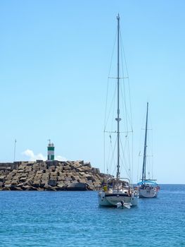 Yachts in the bay near the embankment with a lighthouse on a sunny day