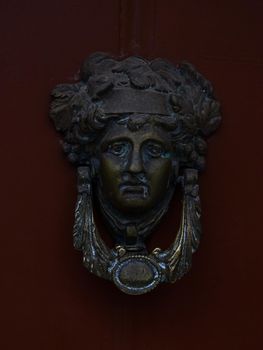 Door knocker in the form of the head of Dionysus on a burgundy wooden door close up