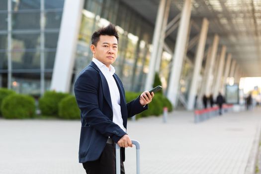 Businessman trying to call a taxi using an app and a mobile phone, asian man at the train station with a big suitcase