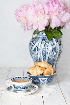 spring still life with croissants and a bouquet of pink luxurious peonies in an ancient Chinese vase with blue ornament, an antique tea cup, early breakfast or brunch, High quality photo