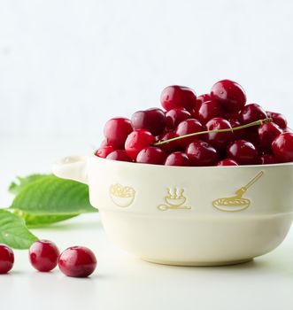 Ripe red cherries in a plate on a white table, close up