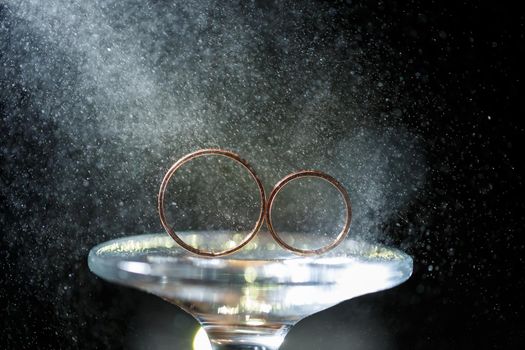 gold wedding rings for newlyweds on a wedding day on a black background with water drops. Jewelry