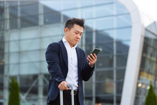 Businessman trying to call a taxi using an app and a mobile phone, asian man at the train station with a big suitcase