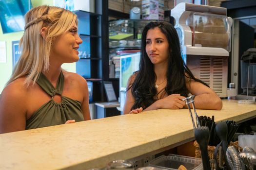 caucasian blond woman drinking spritz close to a latino woman drinking cola drink at the pub.