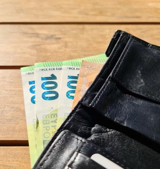 A black leather wallet containing several 100 euro banknotes 