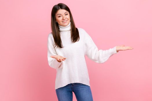 Young girl raised hands as if sharing, gives for free, offers something with friendly generous face, wearing white casual style sweater. Indoor studio shot isolated on pink background.